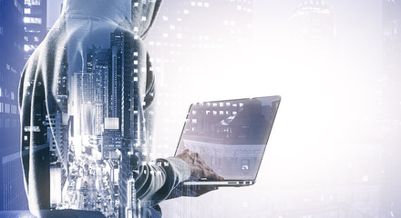 Double exposure of hacker silhouette working with laptop on the background of the city, hacking and crime concept