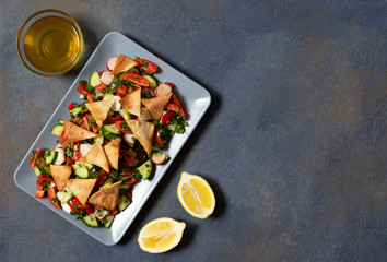 Traditional Fattoush salad  with vegetables and pita bread. Levantine, Arabic, Middle Eastern cuisine. Served in a rectangular plate with lemon and olive oil. Dark background. Top view. Space for text