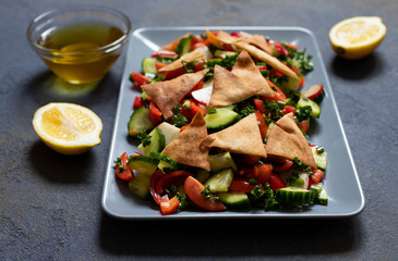 Traditional Fattoush salad  with vegetables and pita bread. Levantine, Arabic, Middle Eastern cuisine. Served in a rectangular plate with lemon and olive oil. Dark background. Close up. Space for text