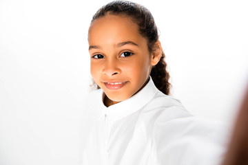 selective focus of smiling african american schoolgirl looking at camera on white background