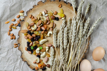 assorted nuts and dried fruits with ears of wheat and eggs on a sawn piece of log
