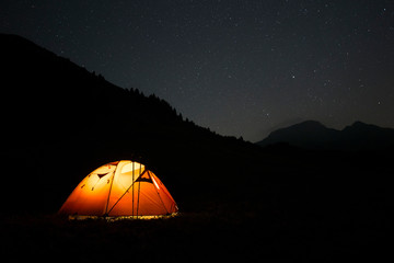 Silhouette of an illuminated trekking tent in high mountain during a starry night