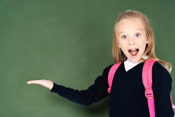 excited schoolgirl looking at camera while standing near green chalkboard