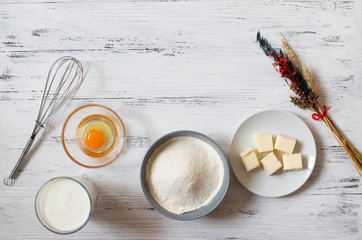 Ingredients for crepes and pancakes on a white wooden background. Flour, egg, milk, butter, whisk. Top view. Space for text.