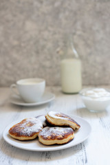 Cottage cheese pancakes, Cheesecakes on the table. Syrniki or sirniki. Healthy breakfast. White dishes. Bottle of milk. A cup of milk. Yogurt or sour cream. White background. Close up