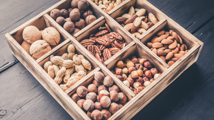 Close-up wooden box with different kinds of nuts on a dark wooden background. Top view