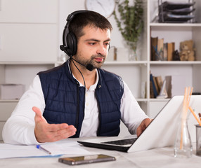 Young male employee with headset and laptop at table