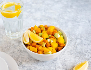 Pegan salad with mango, avocado and sweet potatoes, served with lemon water. Paleo diet. Pegan diet. Vegetarian food. Light background