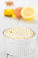 Mayonnaise sauce in white bowl with its ingredients (oil, egg and lemon) in the back (Selective Focus, Focus in the middle of the mayonnaise)