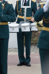 A wind instrument parade - man in green costume standing on the street and playing drums