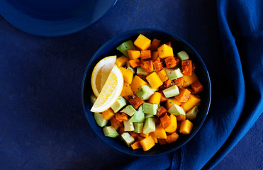 Pegan salad with mango, avocado and sweet potatoes, served with lemon water. Paleo diet. Pegan diet. Vegetarian food. Dark blue background