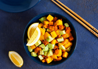 Pegan salad with mango, avocado and sweet potatoes, served with lemon water. Paleo diet. Pegan diet. Vegetarian food. Dark blue background
