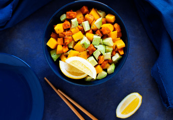 Pegan salad with mango, avocado and sweet potatoes, served with lemon water. Paleo diet. Pegan diet. Vegetarian food. Dark blue background