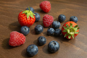 Strawberries, raspberries and blueberries lie on a wooden table