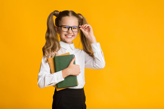 Happy school girl holding books over yellow background, studio shot
