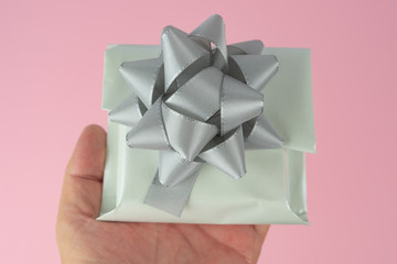 Woman holds a white wrapped gift with silver bow in her hand, pink background