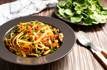 Traditional Italian seafood spaghetti pasta  with mussels served on a dark rustic wooden table with salad. Close-up view