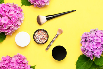 Obraz na płótnie Canvas Set of decorative cosmetics makeup brushes, blush face balls, pink hydrangea flowers on yellow background top view Flat lay copy space. Beauty blogger concept. Fashion background. Makeup accessories