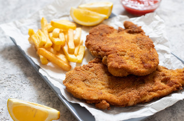 Traditional chicken schnitzel served with french fries, sauce and lemon. Light background. Close-up view