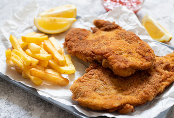 Traditional chicken schnitzel served with french fries, sauce and lemon. Light background. Close-up view