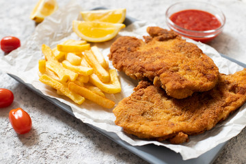 Traditional chicken schnitzel served with french fries, sauce and lemon. Light background. Close-up view