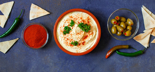 Healthy homemade hummus served with paprika powder, pita bread, olives and parsley. Middle Eastern cuisine, Israeli cuisine, Levanese cuisine, Levantine cuisine. Dark background. Top view