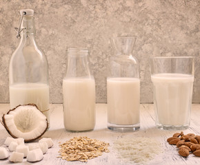 Assortment of healthy organic vegan milk. Almond, rice, oat and coconut milk. Light wooden background. Front view. Toned photo