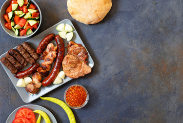 Traditional Serbian and Balkan grilled meat called mesano meso. Balkan barbeque (rostilj) served with Serbian salad, hot peppers, bread, tomato, onions, and paprika powder. Dark background. Top view