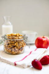 Homemade granola in a glass jar on a light background. Ingredients for a healthy breakfast - granola, apple, strawberry and milk. Close-up