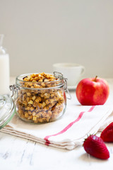 Homemade granola in a glass jar on a light background. Ingredients for a healthy breakfast - granola, apple, strawberry and milk. Close-up