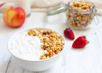 Homemade granola in a glass jar on a light background. Ingredients for a healthy breakfast - granola, apple, strawberry and milk. Close-up