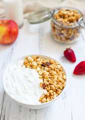 Homemade granola in a glass jar on a light background. Ingredients for a healthy breakfast - granola, apple, strawberry and milk. Close-up