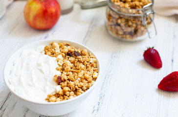 Homemade granola in a glass jar on a light background. Ingredients for a healthy breakfast - granola, apple, strawberry and milk. Close-up