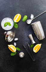 Cocktail shaker and bar tools. Ingredients for a cold alcoholic cocktail. Mojito cocktail. Lemon, mint, ice, rum. Top view, vertical, black background, copy space