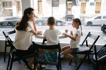 Mother with children drinking hot chocolate and latte at a local coffee shop. They are smiling and having fun.