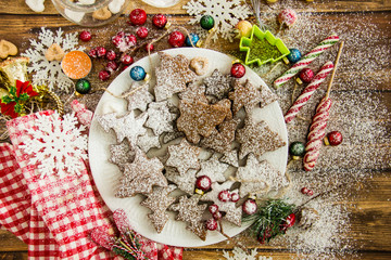Christmas sweets and decorations on table Top view of plate of fresh gingerbread cookies with powdered sugar placed on wooden table amidst various Christmas decorations