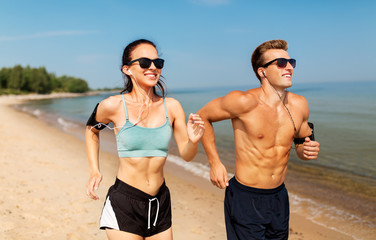 Fototapeta premium fitness, sport and technology concept - happy couple with earphones and arm bands running along summer beach