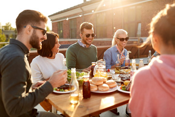 Fototapeta na wymiar leisure and people concept - happy friends having dinner or barbecue party and eating on rooftop in summer