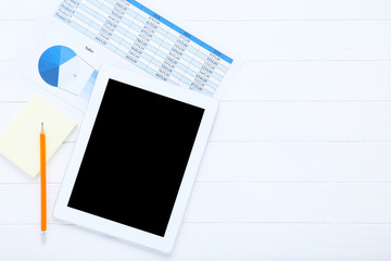 Tablet computer and papers with graph and charts on wooden table
