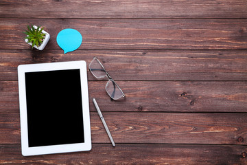 Tablet computer with glasses, pen and green plant on brown wooden table