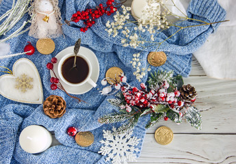 Fototapeta na wymiar Blue knitted sweater, white cup with coffee, homemade cookies, white candles, snowflakes on a light wooden table, top view, flat lay. The concept of a New Year card, Christmas holidays. Save space