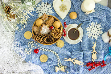 Blue knitted sweater, white cup with coffee, homemade cookies, white candles, snowflakes on a light wooden table, top view, flat lay. The concept of a New Year card, Christmas holidays. Save space