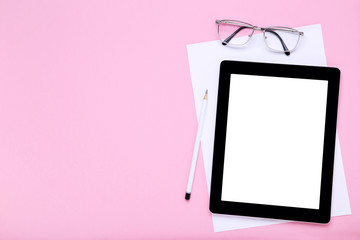 Tablet computer with glasses, pencil and white sheet of paper on pink background