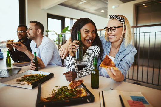 Two businesswomen laughing over pizza and beers after work