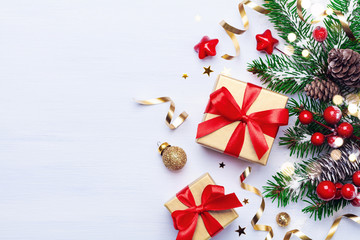 Beautiful Christmas composition on white background with golden Christmas gift boxes, snowy fir branches, conifer cones, holiday decoration and red berry. Top view.