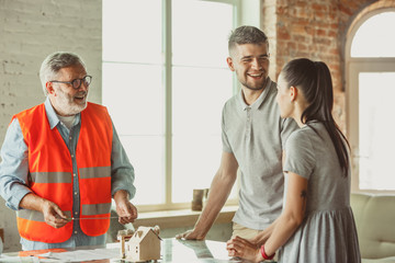 Obraz premium Foreman or achitect engineer shows future house, office or store design plans and model to a young couple. Meeting at the construction office to talk about facade, interior decoration, home layout.