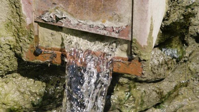 Close up of whater in slow motion flowing out of a wall opening