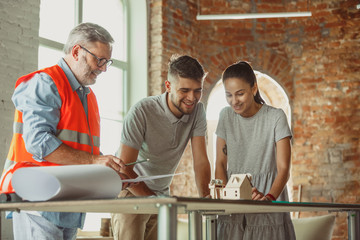 Foreman or achitect engineer shows future house, office or store design plans and model to a young couple. Meeting at the construction office to talk about facade, interior decoration, home layout.