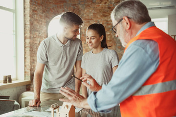 Foreman or achitect engineer shows future house, office or store design plans and model to a young couple. Meeting at the construction office to talk about facade, interior decoration, home layout.