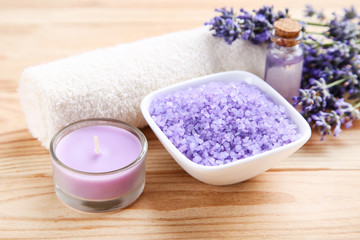 Lavender flowers with oil in bottle, salt in bowl and candle on brown wooden table
